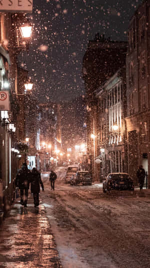 夜間城市街道上飄雪，有發光的街燈和行人。