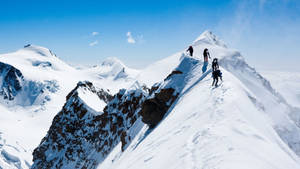 四位登山者在晴朗藍天下攀登積雪山脊。