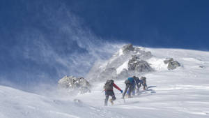 四位登山者在有風的條件下走在積雪的山坡上。
