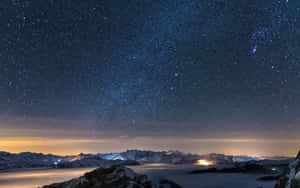 雪覆蓋的山峰在繁星點點的夜空下，下方山谷燈光閃爍。