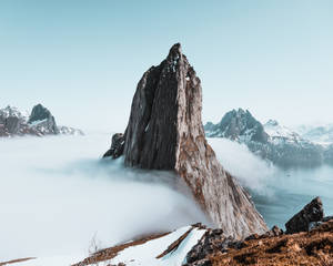 一座戲劇性的山峰聳立於雲層之上，頂部積雪，下方有水。 — 雲朵 壁紙