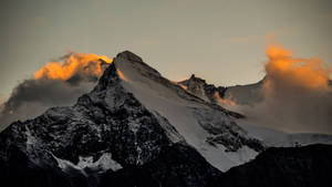 暮色中白雪覆蓋的山峰，金色雲彩在山頂周圍發光。