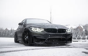 黑色BMW M4在雪中飄移，背景有積雪的房屋和樹木。 — 冬天 壁紙
