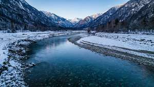 一條蜿蜒的河流流經白雪覆蓋的山谷，河水清澈湛藍，河岸白雪皚皚。