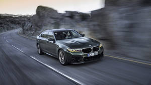 一輛灰色的BMW M5在岩石峭壁模糊的山路上疾馳。