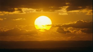 金色夕陽在雲層後落下，映照著黑暗的山丘