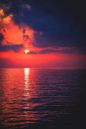 海洋上的夕陽，熾熱的紅色和橙色天空反射在水面上。