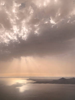 陽光穿過暴風雲，照耀在平靜的海面和遠處的陸地上。