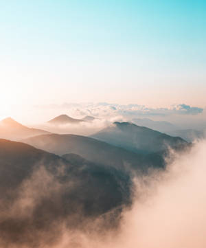 霧氣籠罩的山峰沐浴在日出光線中，柔和的粉彩雲朵在山脊間飄移。 — Galaxy Z Fold 5 壁紙