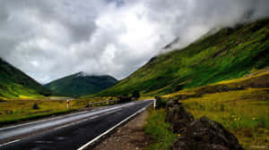 蜿蜒的道路穿過綠色山脈，天空多雲，有霧。