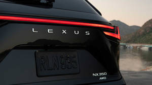 黑色Lexus NX 350 AWD車尾視角，紅色尾燈，靠近水和山，黃昏時分。