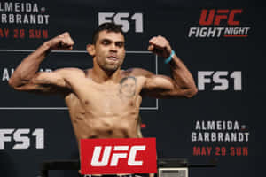 UFC拳手在稱重活動中彎曲手臂，帶有FS1品牌標誌。 — 運動 壁紙