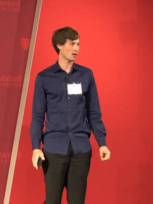 男子在Stanford Medicine活動中穿著海軍藍襯衫和名牌進行演示。