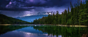 平靜的湖面反射積雪的山峰和昏暗的雲，在黃昏時分。