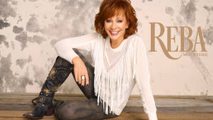 Reba McEntire 身穿白色流蘇毛衣和鉚釘靴，在木樓梯上微笑。