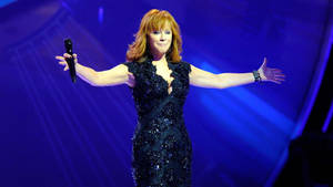 歌手 Reba McEntire 在舞台上穿著黑色亮片連衣裙，雙臂伸展表演。