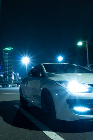 白色跑車停在夜晚的城市街道上，車頭燈和街燈明亮。