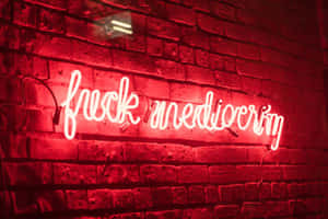 夜間磚牆上寫著「fuck mediocrity」的紅色霓虹燈牌。
