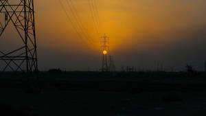 輸電塔在發光的橙色夕陽天空下呈現剪影。