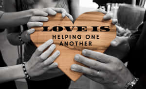 多隻手托住一個木製心形，上面有「Love is helping one another」的訊息。