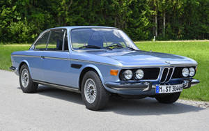 經典藍色BMW 3.0 CSL停泊在靠近綠草和樹木的道路上。