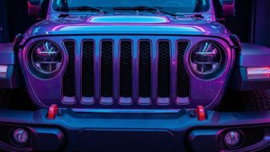 Jeep Wrangler 前格柵喺黑暗嘅工作室中被紫色同藍色霓虹燈光照亮。