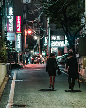 兩個人在雨夜中走在一條霓虹燈照亮的韓國城市街道上。 — 夜景城市 壁紙