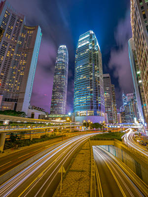 夜間城市場景，有燈火通明的摩天大樓和流動的車燈。