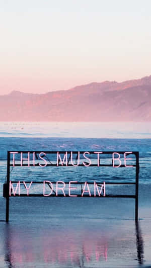 霓虹燈牌寫著「THIS MUST BE MY DREAM」，在日落時分的海水中。