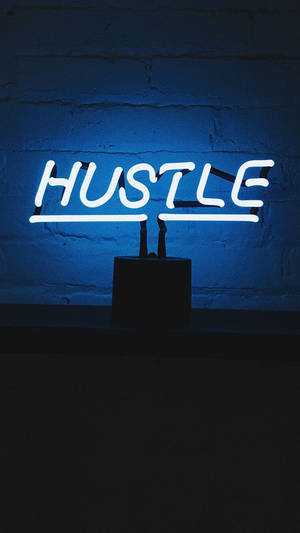 一個發光的白色霓虹燈牌，在藍色磚牆上寫著 HUSTLE。 — 霓虹 iPhone 壁紙