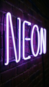 一個紫色霓虹草書招牌，在深色磚牆上寫著「NEON」。 — 霓虹美學 壁紙
