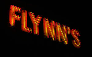 霓虹燈牌寫著 Flynn's，在黑暗的夜晚背景下發出橙色和紅色的光芒。