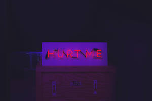 黑暗房間中木箱上寫著 hurt me 的紅色霓虹燈牌。