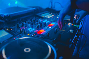 DJ的手在藍色燈光下調整音樂混音器上的發光控制。