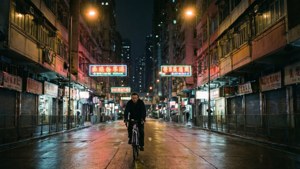 一個人在夜晚騎單車行駛在潮濕的城市街道上，下方是發光的霓虹招牌。