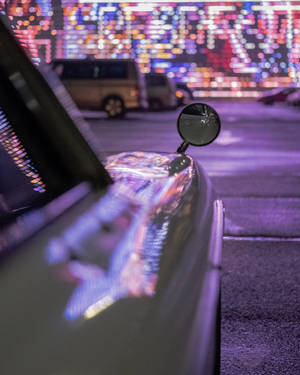 汽車側鏡和引擎蓋在夜晚反射出多彩的城市燈光。 — 酷車 壁紙