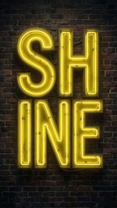 一個黃色霓虹燈牌，上面寫著SHINE，安裝在深色磚牆上。
