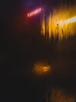 窗戶上的雨痕反射著城市夜晚的霓虹燈光。 — 螢光黃 壁紙