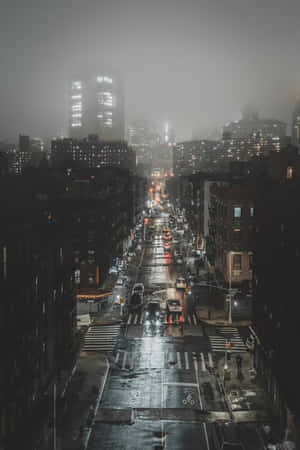 夜晚一條潮濕的城市街道，閃爍的車燈和遠處霧濛濛的摩天大樓。