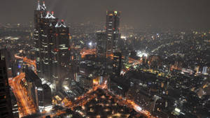 密集市區的夜間鳥瞰圖，燈火通明的摩天大樓和街道。