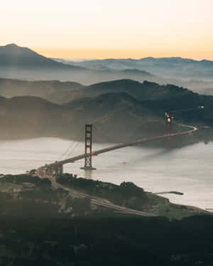 日落時的金門大橋，霧氣籠罩的山丘和寧靜的水面。