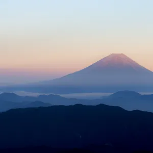 富士山沐浴在粉紅色的黎明光芒中,籠罩在霧氣繚繞的山脈之上。