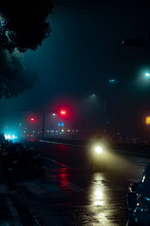 電單車手在夜間濕滑的城市街道上，紅色交通燈穿過霧氣閃爍。
