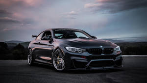 黑色BMW M4跑車在黃昏時停在路上，後面有山丘