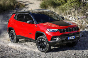 紅色Jeep Compass在碎石路上行駛，塵土飛揚