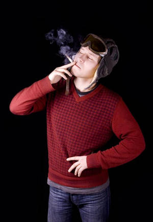穿著紅色毛衣和飛行員帽的男人抽煙，煙霧上升。