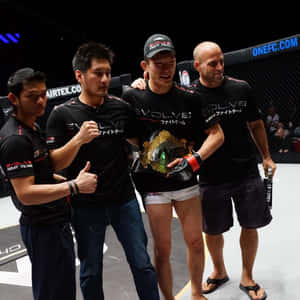MMA拳手與冠軍腰帶和團隊在八角籠內慶祝勝利。 — 動漫打鬥 壁紙