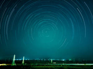 星軌在青綠色夜空下，在電線和城市燈光之上旋轉。