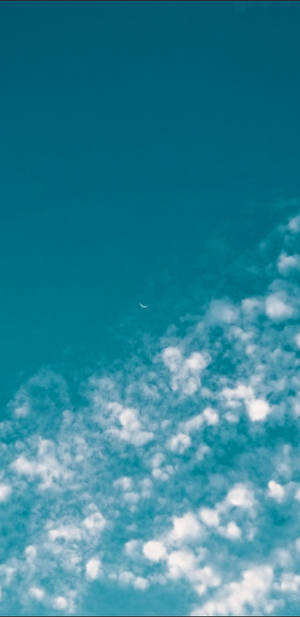 彎月位於蓬鬆白雲之上，背景為藍綠色天空