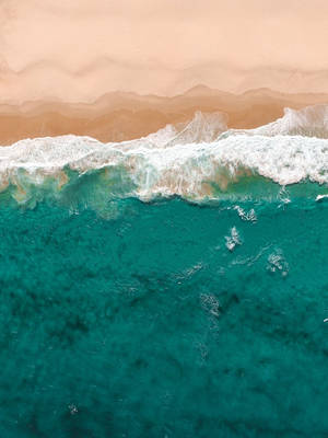 從上方觀看，碧綠色的海浪湧向蜜桃色的沙灘。 — 青綠色 GIF 壁紙